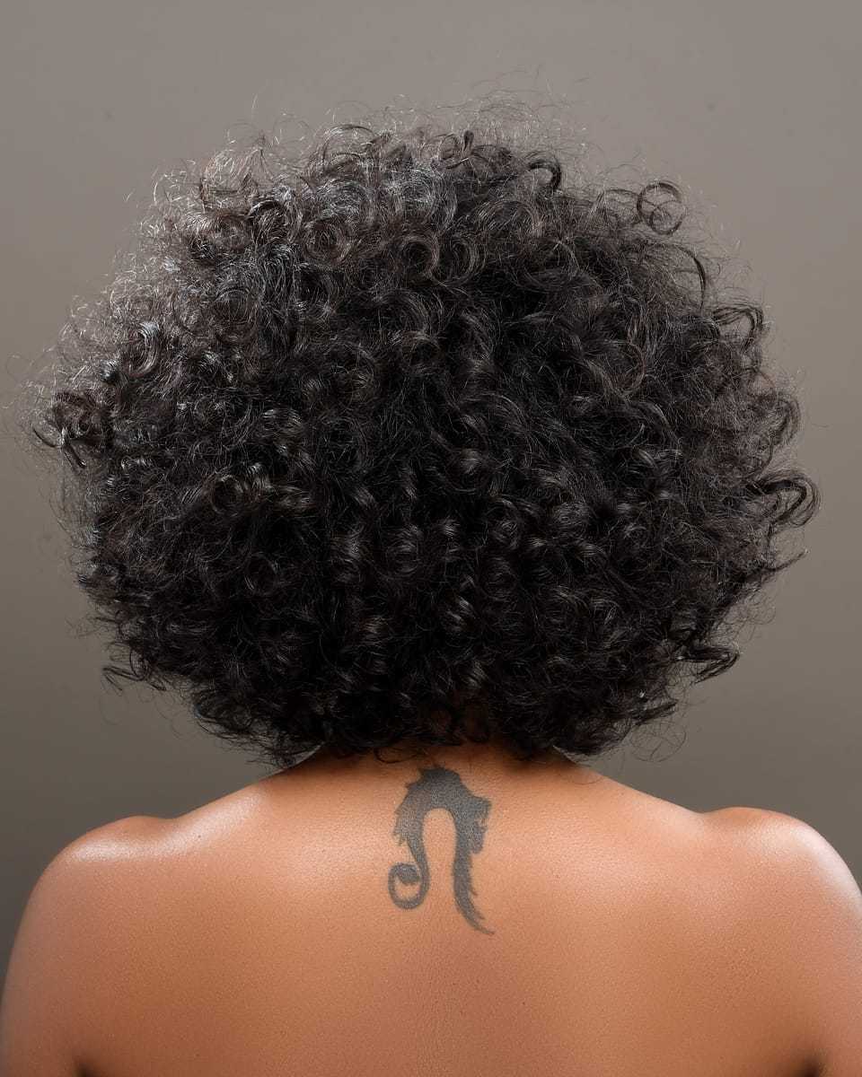 Curly-haired woman with seahorse tattoo on back, facing away.
