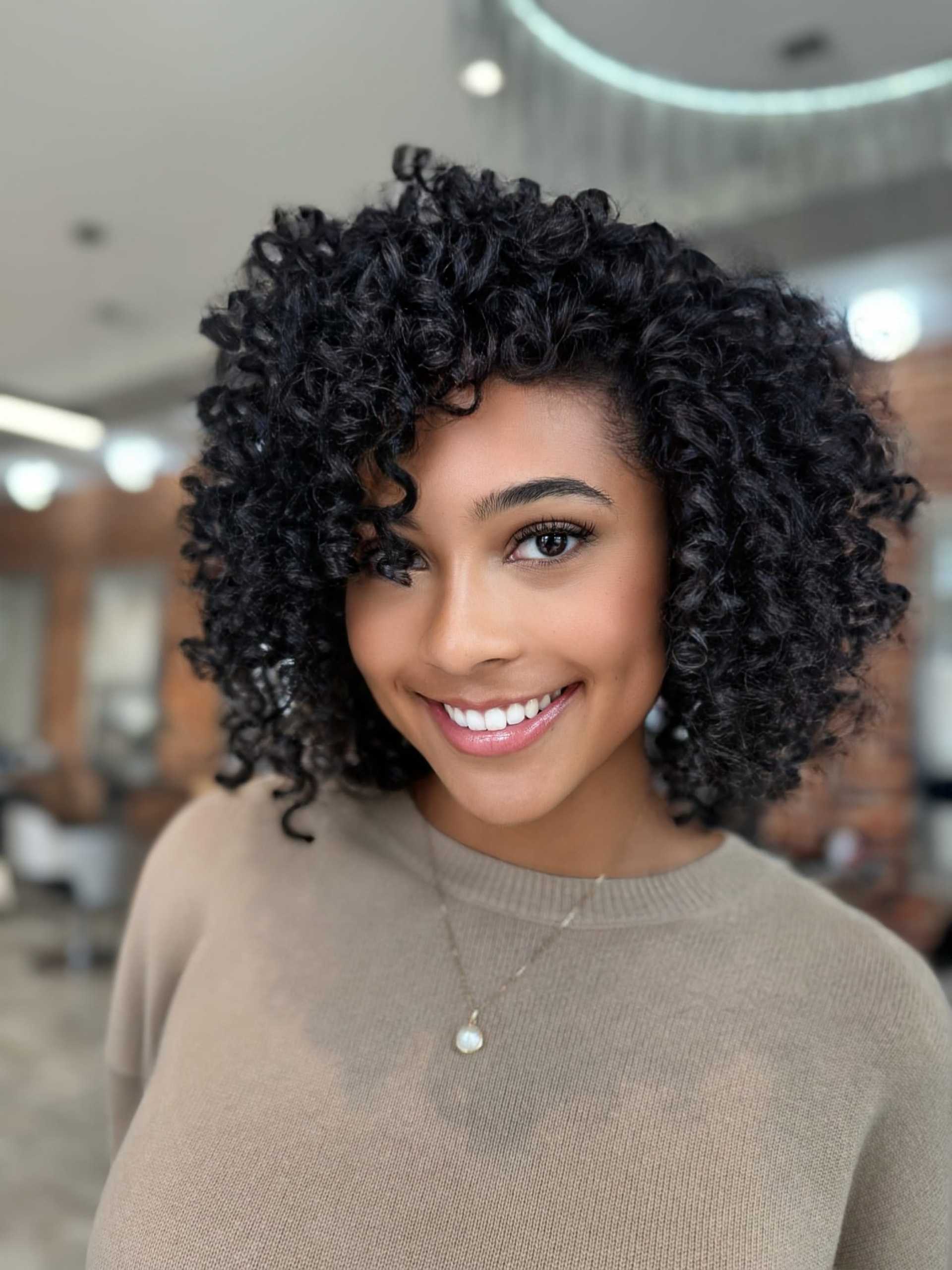 Smiling person with curly hair in a stylish indoor setting.