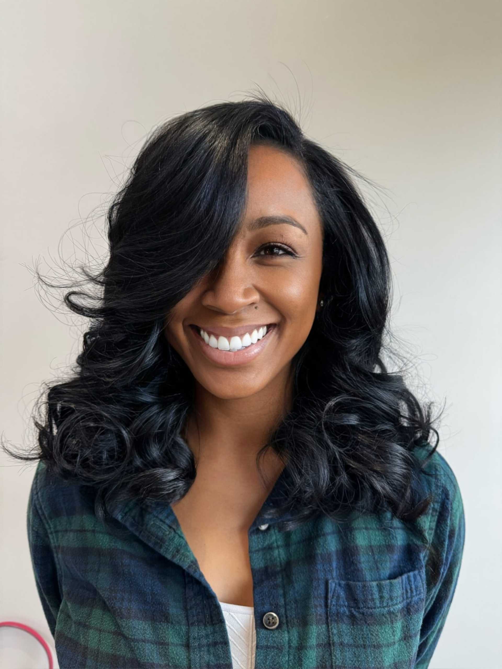Smiling person with long wavy hair wearing a plaid shirt against a plain background.