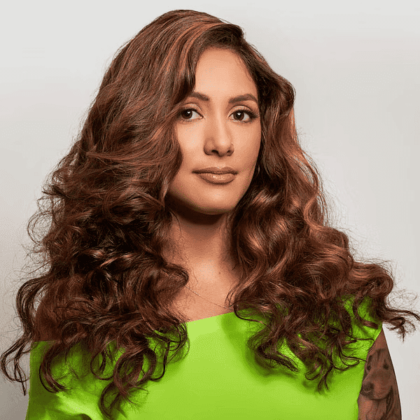 Woman with long, curly hair in a bright green top, showing a tattoo on her upper arm.