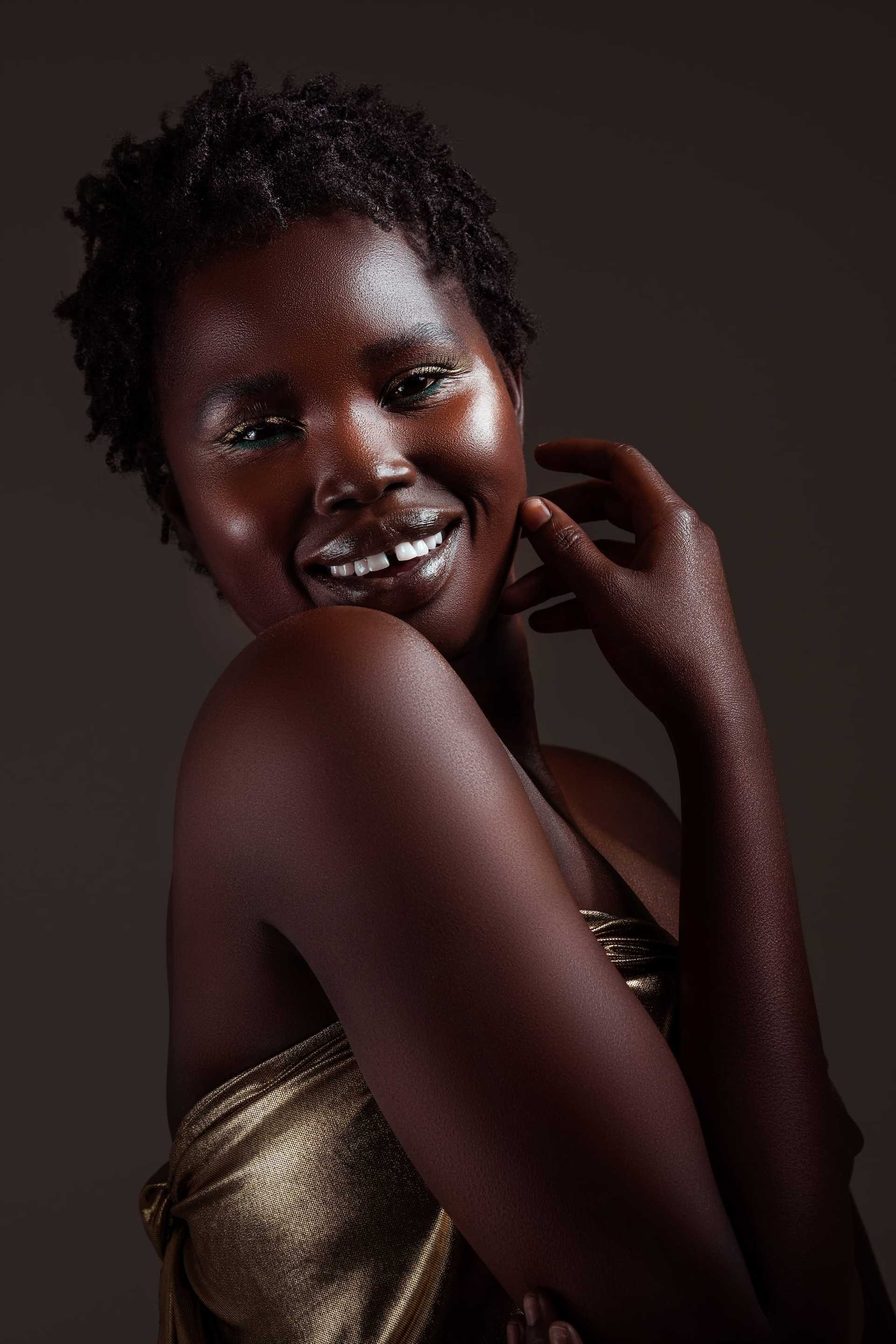 Smiling person in golden attire against a dark background, with a happy, expressive pose.