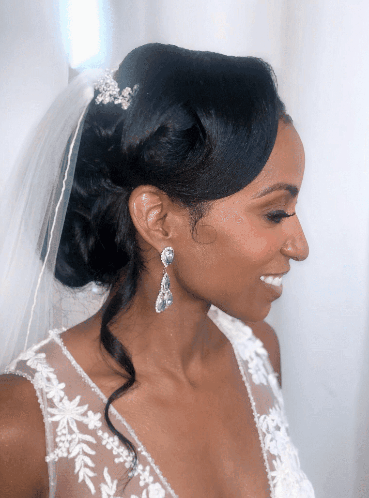 Bride smiling in elegant gown with intricate lace and silver earrings.